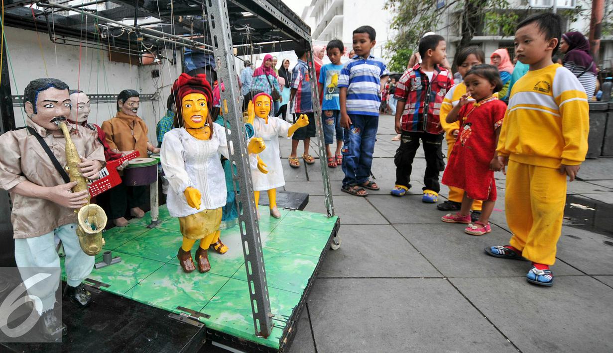 Sebuah gerobak kayu dengan genset serta sound system seadanya tampak dikerubungi anak-anak yang terlihat penasaran melihat 8 boneka kayu menari mengikuti irama musik di pelataran Museum Fatahillah, Jakarta, Kamis (17/12/2015). (Liputan6.com/Yoppy Renato)