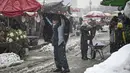 Seorang pria menutupi dirinya dengan selendang saat hujan salju lebat di sebuah pasar di Kabul (4/1/2022). Sedikitnya tujuh warga Afghanistan tewas dan 26 lainnya cedera dalam beberapa kecelakaan lalu lintas. (AFP/Mohd Rasfan)