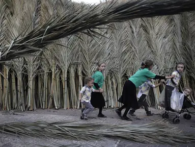 Anak-anak bermain di dekat seorang pria Yahudi Ultra-Ortodoks yang membawa daun pohon palem di Yerusalem (1/10). Hari Raya Sukkot merupakan salah satu hari raya besar umat Yahudi yang dalam bahasa Ibrani disebut Tabernakel. (AFP Photo/Manahem Kahana)