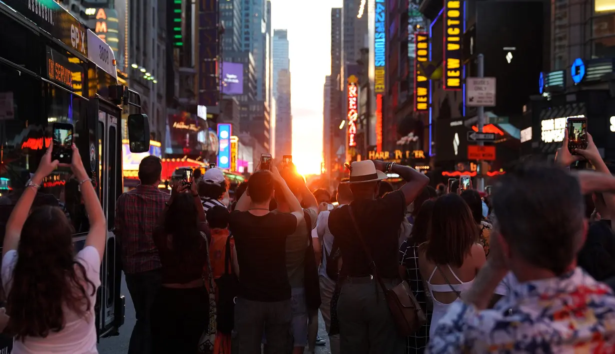 Orang-orang mengambil gambar fenomena Manhattanhenge, dimana matahari terbenam sejajar tepat dengan jalan, di 42nd street di Times Square, New York City, Kamis (12/7). Fenomena ini hanya terjadi selama beberapa hari dalam setahun. (AFP/TIMOTHY A. CLARY)