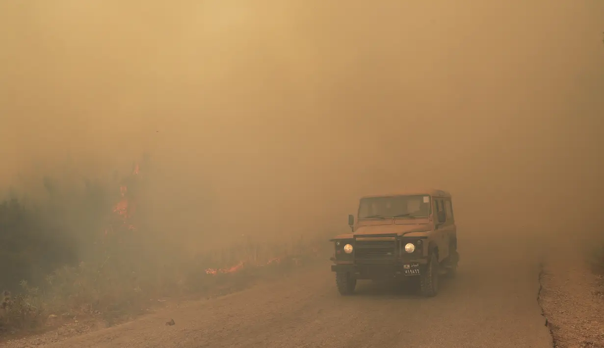 Sebuah kendaraan tentara Lebanon melewati kobaran api kebakaran hutan, di desa Qobayat, di utara provinsi Akkar, Lebanon, Kamis (29/7/2021). Setidaknya satu petugas pemadam kebakaran tewas dalam memadamkan api. (AP Photo/Hussein Malla)
