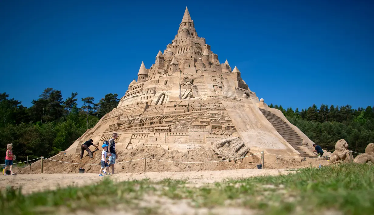 Pengunjung melintasi di depan istana pasir tertinggi pada kompetisi tahunan "Sand Sculptures Festival" di Binz, Pulau Reugen di Laut Baltik, Jerman, 5 Juni 2019. Istana pasir buatan Thomas van Dungen ini dibuat persis seperti istana yang ada di serial film Game of Thrones. (Jens Büttner/dpa/AFP)