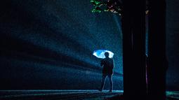 Pengunjung memakai payung saat berada di dekat seni instalasi cahaya "Painting the Night" karya seniman Austria Victoria Coeln saat hujan turun di taman Heruerhae Gaerten di Hanover, Jerman utara, (4/5). (AFP Photo/dpa/Silas Stein/Jerman Out)