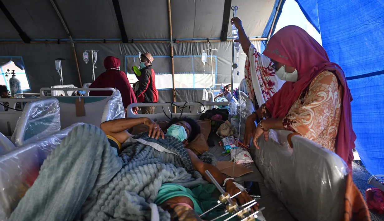 Orang-orang yang terluka dalam gempa dengan magnitudo 6,2 menerima perawatan di tempat penampungan sementara di luar Rumah Sakit Regional Sulbar, Mamuju, Sulawesi Barat, Minggu (17/1/2021). Mereka dirawat di dalam tenda darurat untuk mengantisipasi gempa susulan. (ADEK BERRY/AFP)