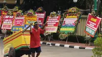 Warga melintasi deretan karangan bunga yang diletakkan di depan Mabes Polri, Jakarta, Rabu (3/5). Ratusan karangan bunga itu terus berdatangan dan mengelilingi gedung Mabes Polri di Jalan Trunojoyo Jakarta Selatan. (Liputan6.com/Helmi Fithriansyah)