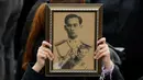 Seorang pelayat wanita memegang foto Raja Bhumibol Adulyadej saat berkumpul di luar Grand Palace sambil menyanyikan rekaman lagu kerajaan untuk menghormati raja mereka, di Bangkok, Thailand, (22/10) (REUTERS/Jorge Silva)