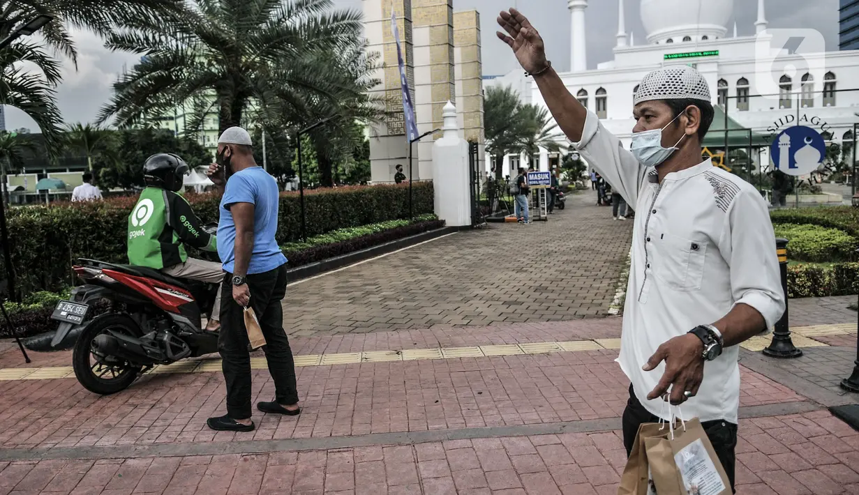 Petugas mengajak pengendara yang melintas mengambil takjil secara drive thru di Kompleks Masjid Al-Azhar, Jakarta, Selasa (13/4/2021). Pengelola Masjid Al-Azhar menyiapkan 500 bungkus takjil per hari yang dibagikan secara drive thru guna mencegah penyebaran COVID-19. (merdeka.com/Iqbal S. Nugroho)