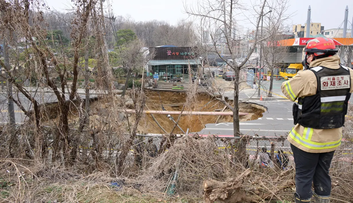 Seorang penyelidik mengambil foto lubang runtuhan di luar sebuah toko tanaman di sebuah jalan di Seoul, Korea Selatan pada tanggal 25 Maret 2025. (Anthony WALLACE/AFP)