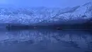 Orang-orang menikmati perjalanan dengan perahu dengan latar belakang pegunungan yang tertutup salju di danau Dal di Srinagar (11/1/2022). Danau Dal di Kashmir bisa dibiland danau terindah di kaki Pegunungan Himalaya. (AFP/Tauseef Mustafa)