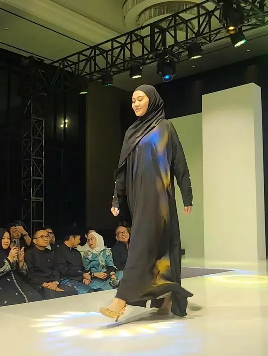 Gaya sederhana nan anggun Aaliyah Massaid dibalut gamis dan hijab pashmina serba hitam saat melenggang di fashion show brand modest milik Thariq Halilintar dan Harris Vriza, Thoiba Concept. [@rezaartemevia.official]