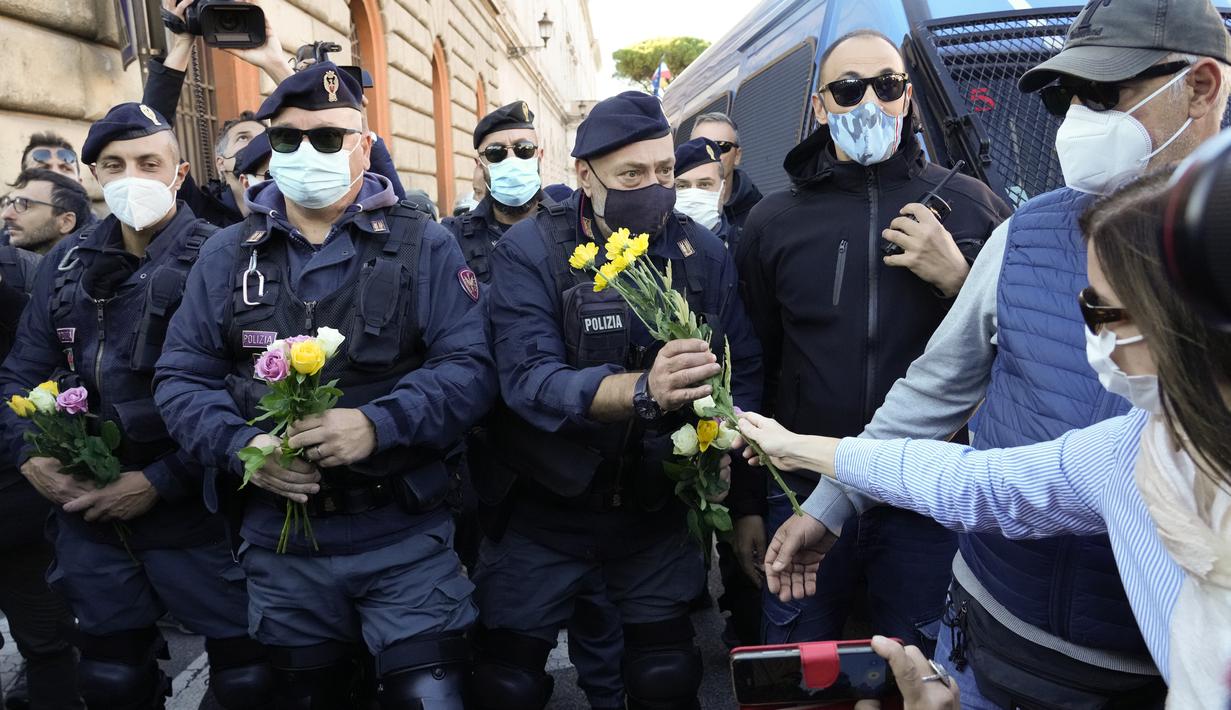 Demonstran membawa bunga untuk petugas polisi selama aksi protes di Circus Maximus Roma, Jumat (15/10/2021). Protes tersebut karena aturan yang mengharuskan seluruh pekerja di Italia menunjukkan kartu kesehatan covid-19 untuk memasuki tempat kerja mereka. (AP Photo/Gregorio Borgia)