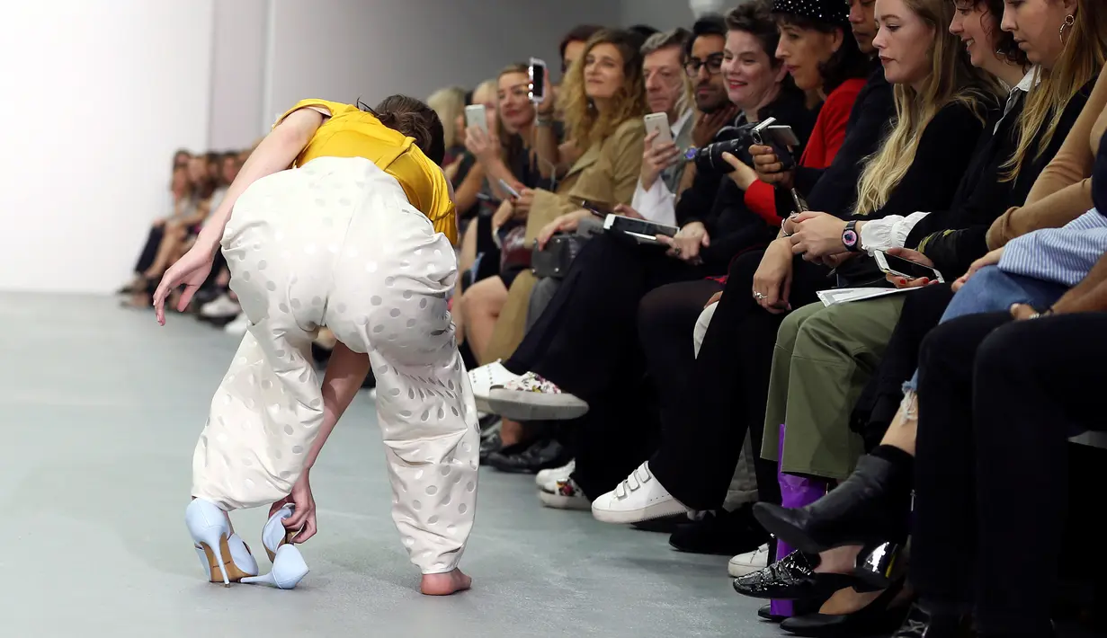 Seorang model membetulkan sepatunya saat memperagakan busana rancangan Emilio De la Morena pada London Fashion Week 2017 di Inggris, Selasa (20/9).  Meski sepatunya terlepas, model ini percaya diri berjalan dengan sebelah alas kaki. (REUTERS/Neil Hall)