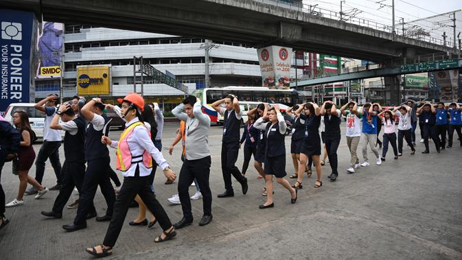 Karyawan pusat perbelanjaan melindungi kepalanya sambil berjalan saat mengikuti latihan gempa di Manila (14/11/2019). Latihan ini sebagai bagian dari kesiapsiagaan nasional menyusul berbagai gempa yang melanda pulau Mindanao bulan lalu. (AFP Photo/Ted Aljibe)