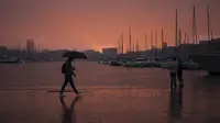 Seorang pria berjalan dengan payung saat pasangan melihat langit di Pelabuhan Vieux Marseille saat badai di Marseille, Prancis selatan, Senin (4/10/2021). Wilayah Prancis selatan dalam siaga untuk hujan lebat dan banjir. (AP Photo/Daniel Cole)