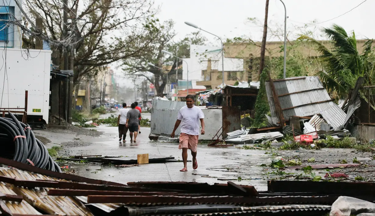 Warga berjalan di samping bangunan yang roboh akibat Topan Mangkhut di kota Tuguegarao di provinsi Cagayan, timur laut Filipina (15/9). Aktivitas sekolah dihentikan sementara dan kantor pemerintahan telah ditutup. (AP Photo/Aaron Favila)