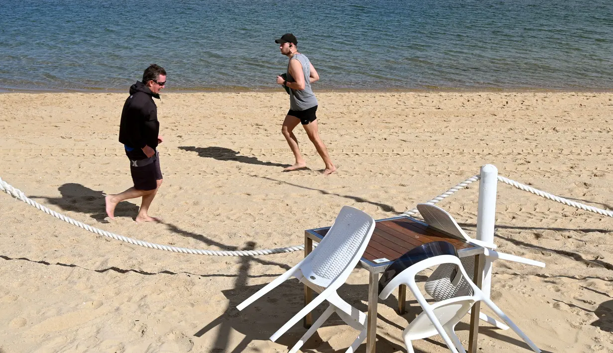 Warga joging melewati meja dan kursi kosong di sebuah pantai di Melbourne, Australia, Kamis (19/8/2021). Melbourne melewati 200 hari dalam lockdown keras sejak dimulainya pandemi COVID-19. (William WEST/AFP)