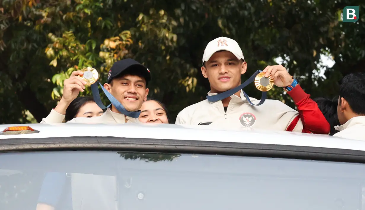 Peraih medali emas Olimpiade Paris 2024, Veddriq Leonardo (kiri) dan Rizki Juniansyah memamerkan medali saat melakukan pawai bersama sejumlah atlet dan ofisial Kontingen Indonesia lainnya menggunakan bus tingkat terbuka Transjakarta menuju Istana Negara, Jakarta Pusat, Kamis (15/8/2024). (Bola.com/Abdul Aziz)