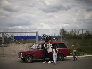 Orlyanske (kiri) memeluk istrinya Kolya di samping mobil mereka saat mereka tiba dari Vasylivka ke pusat penerimaan pengungsi di Zaporizhzhia, Ukraina, Selasa (3/5/2022). Ribuan warga Ukraina terus meninggalkan wilayah yang diduduki Rusia. (AP Photo/Francisco Seco)