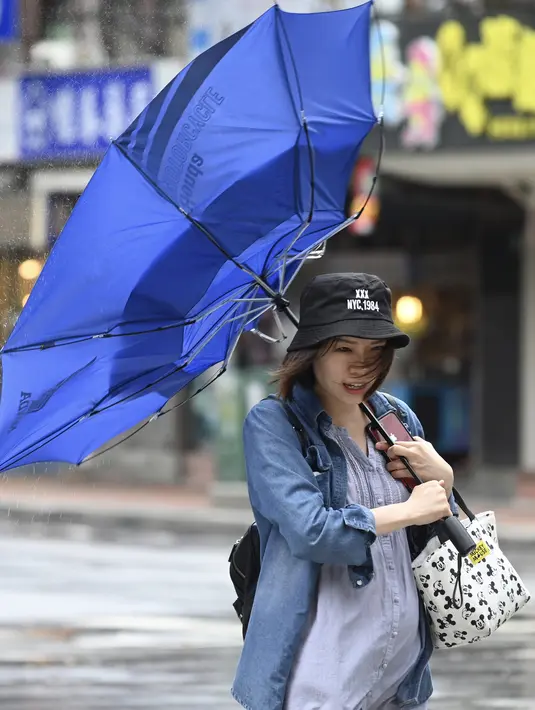 Seorang wanita membawa payungnya yang rusak saat berjalan melawan angin kencang yang ditimbulkan oleh topan Lekima di Taipei, Taiwan (9/8/2019). Topan  tersebut dinilai sebagai yang terkuat menghantam Taiwan di tahun ini. (AFP Photo/Sam Yeh)