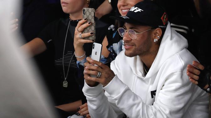 Pemain PSG, Neymar bermain ponsel saat menghadiri acara peragaan busana Off-White Spring-Summer 2019 Ready-to-Wear selama Paris Fashion Week, Prancis (27/9). Neymar tampil mengenakan jaket putih dan kaca mata emas. (AFP Photo/Francois Guillot)