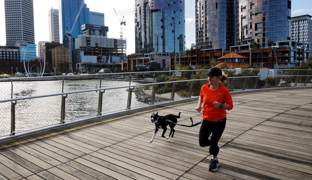 Seorang wanita berlari dengan anjingnya melalui Elizabeth Quay di Perth (29/6/2021). Kota ini mengikuti Sydney dan Darwin melakukan lockdown untuk menahan wabah baru varian Delta yang sangat menular. (AFP/Trevor Collens)