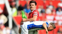 Bek Manchester United, Harry Maguire, mengangkat kaki pemain Brighton and Hove Albion, Leandro Trossard, pada laga Liga Inggris di Stadion Old Trafford, Minggu (07/08/2022). (AP/Lindsey Parnaby)