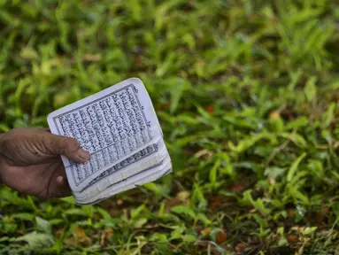 Seorang perempuan membaca Alquran pada peringatan 16 tahun gempa bumi dan tsunami Aceh di sebuah kuburan massal di Siron, Sabtu (26/12/2020).  Peringatan di tengah pandemi COVID-19 itu tetap berlangsung secara sederhana melalui kegiatan ziarah kubur. (CHAIDEER MAHYUDDIN/AFP)