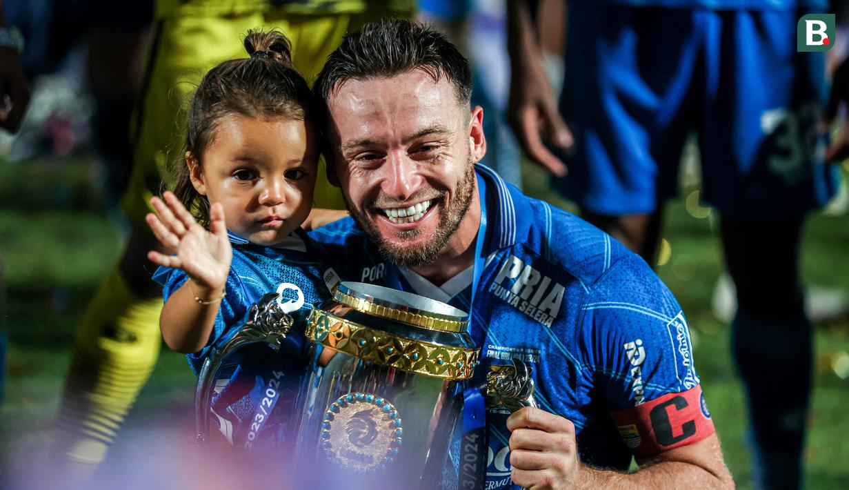 Selebrasi gelandang Persib Bandung, Marc Klok dengan trofi juara bersama sang putri, Sage Luan Klok dalam perayaan gelar juara Championship Series BRI Liga 1 2023/2024 setelah mengalahkan Madura United 3-1 pada laga final leg kedua di Stadion Gelora Bangkalan, Madura, Jumat (31/5/2024). (Bola.com/Bagaskara Lazuardi)