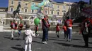 Seorang anak memegang balon saat melihat pekerja taman hiburan memegang komidi putar sementara mereka bergabung dengan pekerja sirkus dalam demonstrasi menuntut dukungan pemerintah Italia karena kegiatan mereka ditutup sejak dimulainya wabah COVID-19, di Roma (26/3/2021). (AP Photo/Gregorio Borgia)