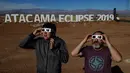 Dua orang pria mencoba kaca mata khusus untuk melihat gerhana matahari total di sebuah kamp astronomi  di komune Vallenar di gurun Atacama, Santiago, Chile (1/7/2019). Gerhana matahari total akan terlihat dari Chile dan Argentina pada 2-3 Juli. (AFP Photo/Martin Bernetti)