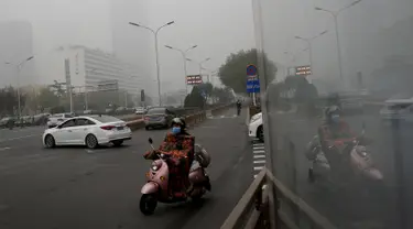 Seorang wanita mengendarai sepeda listrik mengenakan masker di sebuah jalan yang diselimuti kabut asap tebal di Beijing, China (14/11). Pihak berwenang mengeluarkan peringatan kuning untuk polusi udara buruk pada hari Rabu. (AP Photo/Andy Wong)