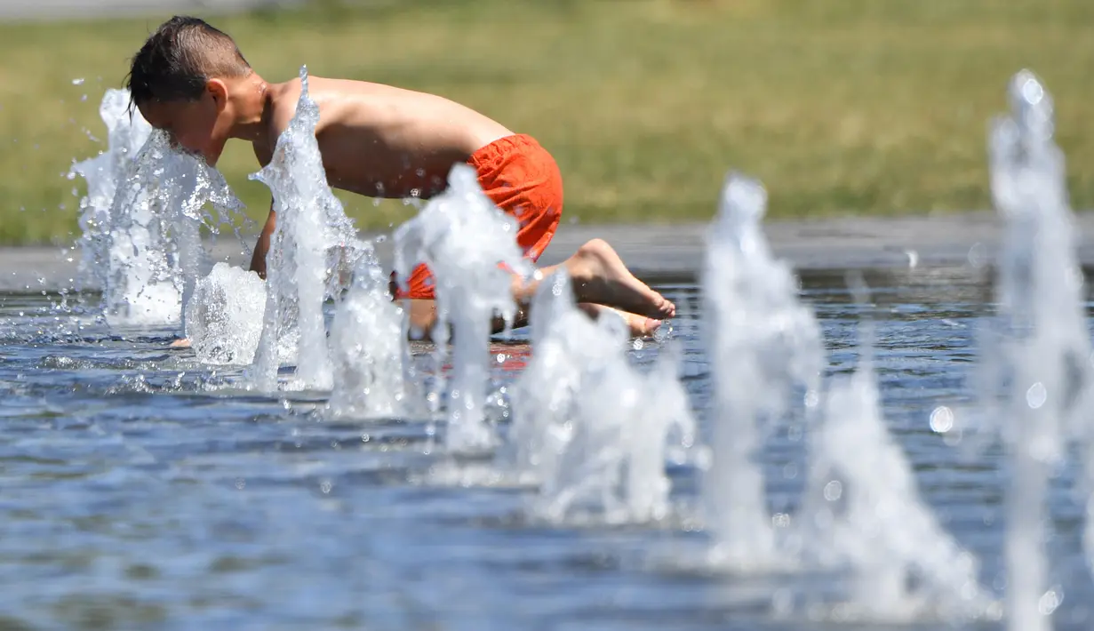 Seorang anak mendekatkan wajahnya pada air mancur saat menikmati musim panas di Nantes, Prancis barat, Senin (19/6). Suhu temperatur di Prancis mencapai 36 derajat celcius. (AFP Photo / LOIC VENANCE)