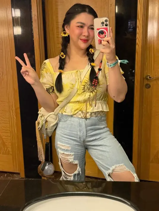 Sementara di hari kedua, Vicky tampil lebih playful dalam balutan ruffle blouse kuning cerah yang dipadukan dengan ripped jeans. Sling bag warna butter dan aksesori bunga matahari di rambut menambah sentuhan ceria pada look-nya. [@vickyshu].