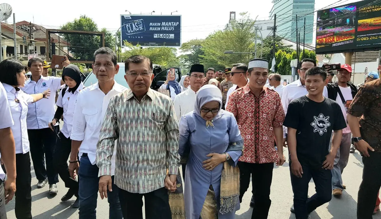 Mantan Wakil Presiden Jusuf Kalla atau JK (kiri) didampingi istrinya Mufidah berjalan kaki saat tiba di kampung halamannya, Makassar, Sulawesi Selatan, Sabtu (26/10/2019). JK disambut meriah warga Makassar. (Liputan6.com/HO/Tim JK)