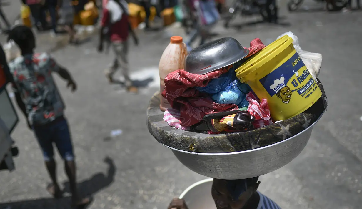 Seorang perempuan membawa baskom dengan barang-barangnya di pasar Petion-Ville di Port-au-Prince, empat hari setelah pembunuhan Presiden Haiti Jovenel Moise, Minggu (11/7/2021). Moïse tewas dibunuh dalam serangan di kediaman pribadinya, pada Rabu 7 Juli 2021 dini hari. (AP Photo/Matias Delacroix)