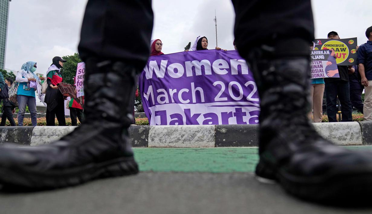 Seorang petugas polisi berjaga-jaga saat para aktivis membentangkan spanduk dalam unjuk rasa Hari Perempuan Internasional di Jakarta, Indonesia, Jumat, 8 Maret 2024. (AP Photo/Dita Alangkara)
