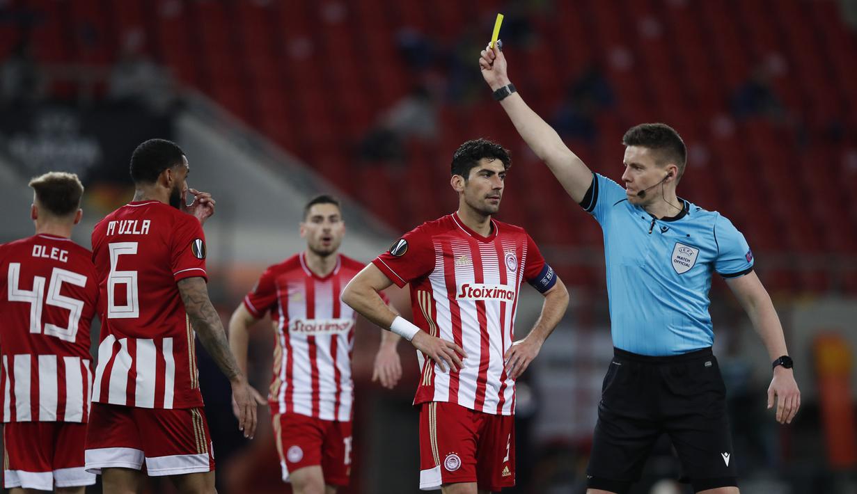 Wasit Daniel Siebert memberikan kartu kuning kepada gelandang Olympiakos, Yann M'Vila (kedua dari kiri) dalam laga leg pertama babak 16 besar Liga Europa 2020/2021 di Georgios Karaiskakis Stadium, Kamis (11/3/2021). Olympiakos kalah 1-3 dari Arsenal. (AP/Thanassis Stavrakis)