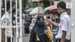 Petugas keamanan memeriksa suhu tubuh orangtua dari anak penerima KJP sebelum memasuki area pengambilan kartu di kawasan Matraman, Jakarta, Selasa (24/11/2020). (merdeka.com/Iqbal S. Nugroho)