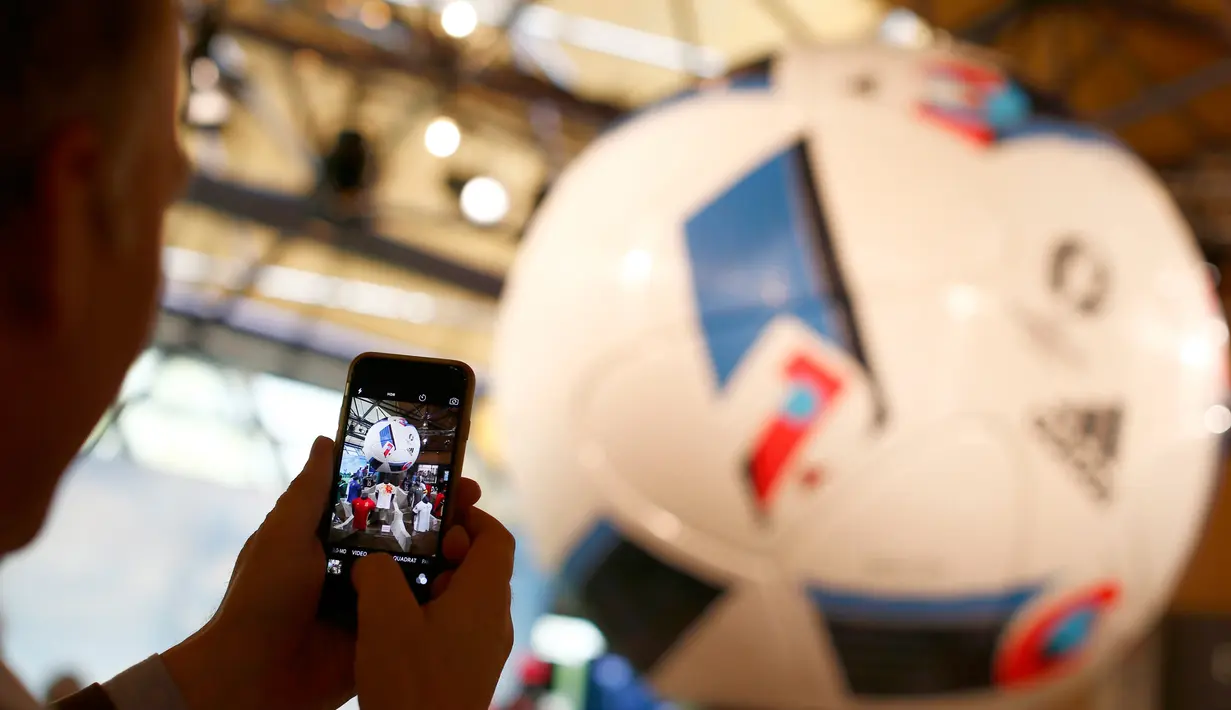 Seorang pengunjung saat mengabadikan Bola resmi gelaran Piala Eropa 2016 di Prancis ditampilkan saat acara  rapat tahunan Adidas di kota Bavarian, Nuremberg , Jerman , 12 Mei 2016. (REUTERS / Michaela Rehle)