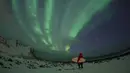 Seorang peselancar berdiri menatap sinar aurora sebelum beraksi di pantai Unstad, Lofoten, Arctic Circle, (10/3/2016). (AFP/Olivier Morin)