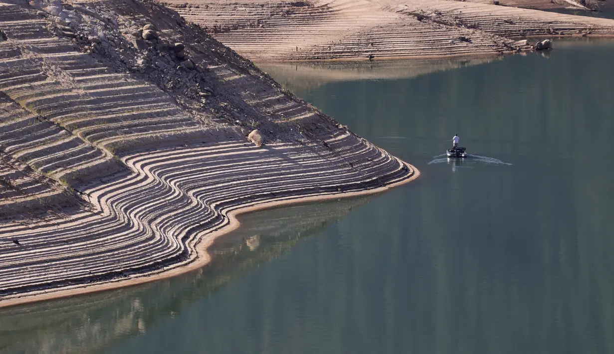 Garis air terlihat di tepi curam Danau Oroville saat seorang nelayan mengapung di Oroville, California (1/6/2021). Volume air waduk Danau Oroville yang terus menyusut saat ini menyisakan kapasitas 38 persen. (AFP/Justin Sullivan)