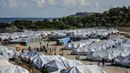 Para migran mengisi air sementara yang lain membersihkan barang-barang mereka setelah hujan badai di kamp pengungsi Kara Tepe, di timur laut pulau Lesbos, Yunani (14/10/2020). (AP Photo/Panagiotis Balaskas)