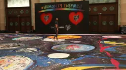 Seniman Inggris Sacha Jafri berpose di atas lukisannya berjudul "The Journey of Humanity" di Dubai, UEA pada 1 Oktober 2020. Donasi dari karya seni ini akan digunakan untuk inisiatif kesehatan dan pendidikan bagi anak-anak yang hidup dalam kemiskinan di seluruh dunia. (AP Photo/Kamran Jebreili)