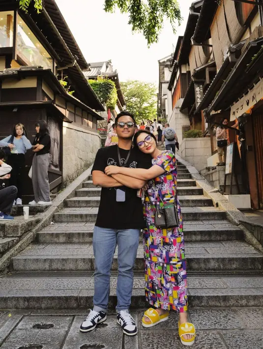 Potret gemas lainnya dari Ashanty saat berlibur di Jepang. Berpose memeluk anak laki-lakinya Azriel Hermansyah, Ashanty tampil dengan set atasan lengan pendek dan rok panjang yang serasi. Set ini memiliki motif abstrak yang ramai, sehingga Ashanty hanya memadukannya dengan sling bag hitam dan sandal kuning. Foto: Instagram.
