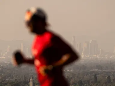 Seorang pelari melintas di depan kabut asap dari berbagai kebakaran hutan di cakrawala pusat kota Los Angeles, Rabu, 11 September 2024. (AP Photo/Etienne Laurent)