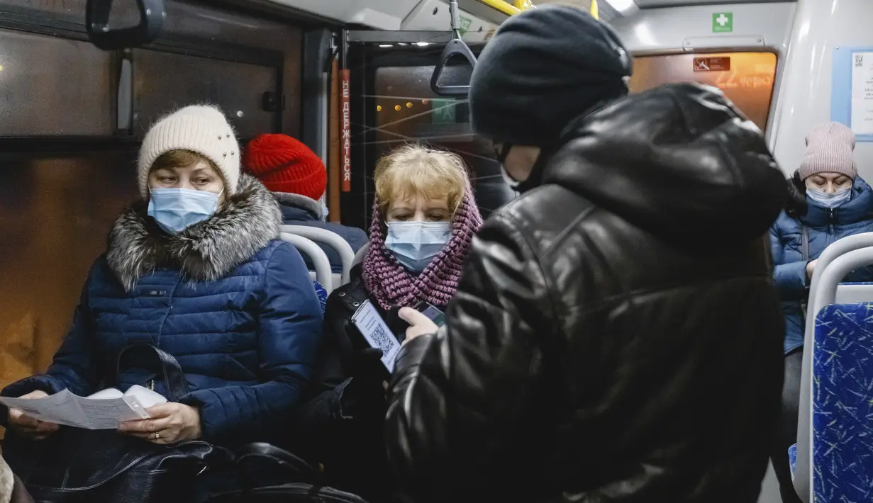 Seorang petugas (kanan) memeriksa kode QR penumpang yang membuktikan tidak adanya infeksi virus corona pada layar ponsel pintar, di dalam bus di Kazan, Senin (22/11/2021). Kazan, menjadi yang pertama di Rusia yang mulai mewajibkan bukti vaksinasi sebelumnya untuk akses transportasi umum. (AP Photo)