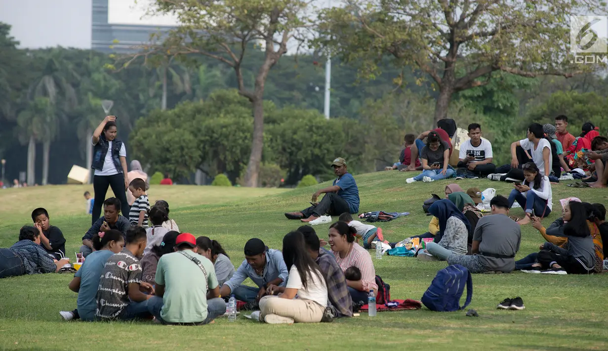 Warga duduk di rumput ketika mengunjungi kawasan Monumen Nasional (Monas) ) saat hari libur Lebaran hari kedua, Jakarta, Kamis (6/6/2019). Monas yang merupakan Ikon Ibu Kota itu menjadi salah satu tujuan wisata untuk mengisi libur Lebaran. (merdeka.com/Imam Buhori)