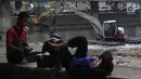 Dua orang pria beristirahat di tepi waduk dengan latar belakang petugas yang sedang mengeruk Waduk Grogol, Jakarta, Senin (9/4). Pengerukan dilakukan untuk mengatasi permasalahan banjir di Ibu Kota. (Liputan6.com/Arya Manggala)