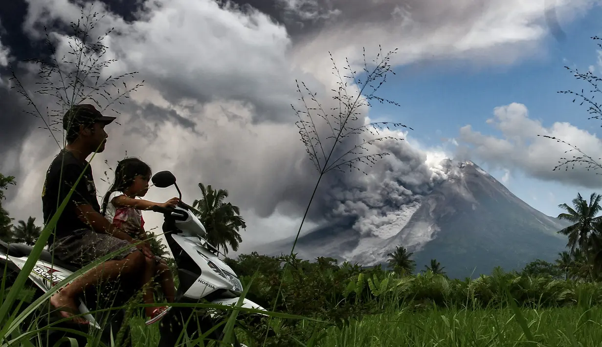 Pengendara motor melintas saat erupsi Gunung Merapi terlihat dari desa Tunggularum di Sleman pada 11 Maret 2023. Berdasarkan pengamatan pada Sabtu (11/3/2023) mulai pukul 06.00-12.00 WIB, BPPTKG mencatat satu kali guguran lava keluar dari Gunung Merapi dengan jarak luncur maksimal 1.500 meter ke arah barat daya. (AFP/Devi Rahman)