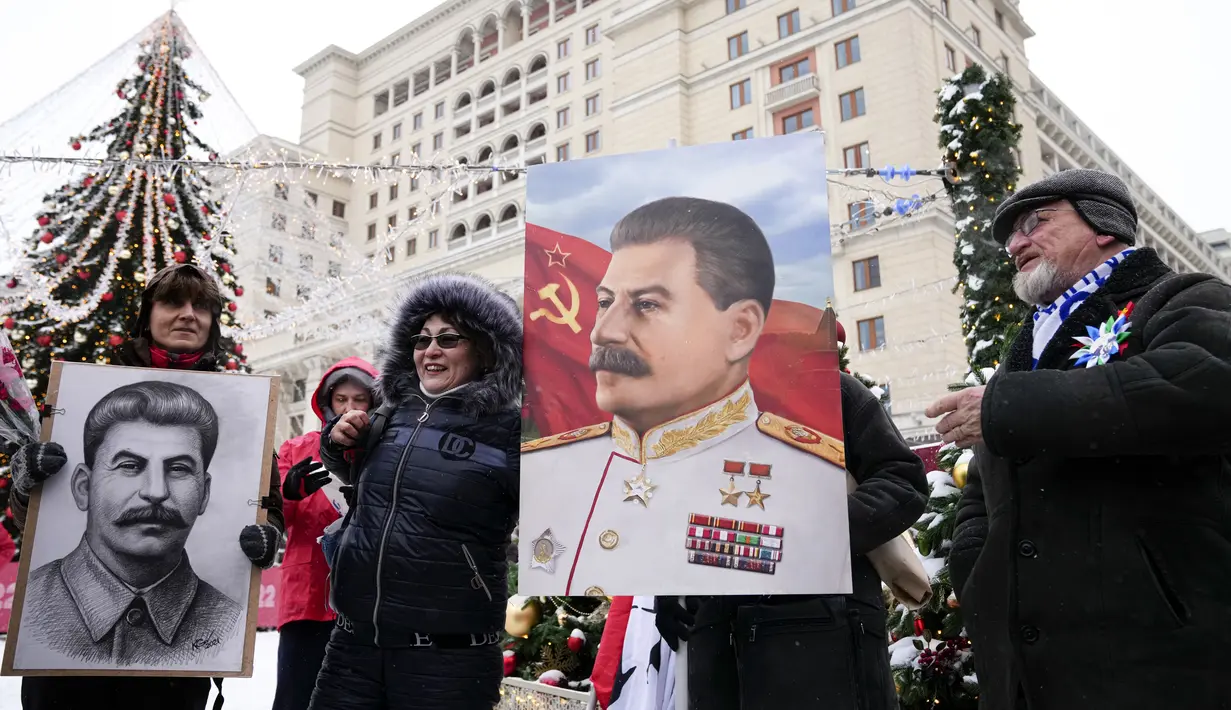 Orang-orang berfoto sambil memegang potret pemimpin Soviet Josef Stalin sebelum meletakkan bunga di makamnya menandai peringatan 142 tahun kelahirannya di dekat Tembok Kremlin di Lapangan Merah di Moskow, Rusia, Selasa (21/12/2021). (AP Photo/Alexander Zemlianichenko)